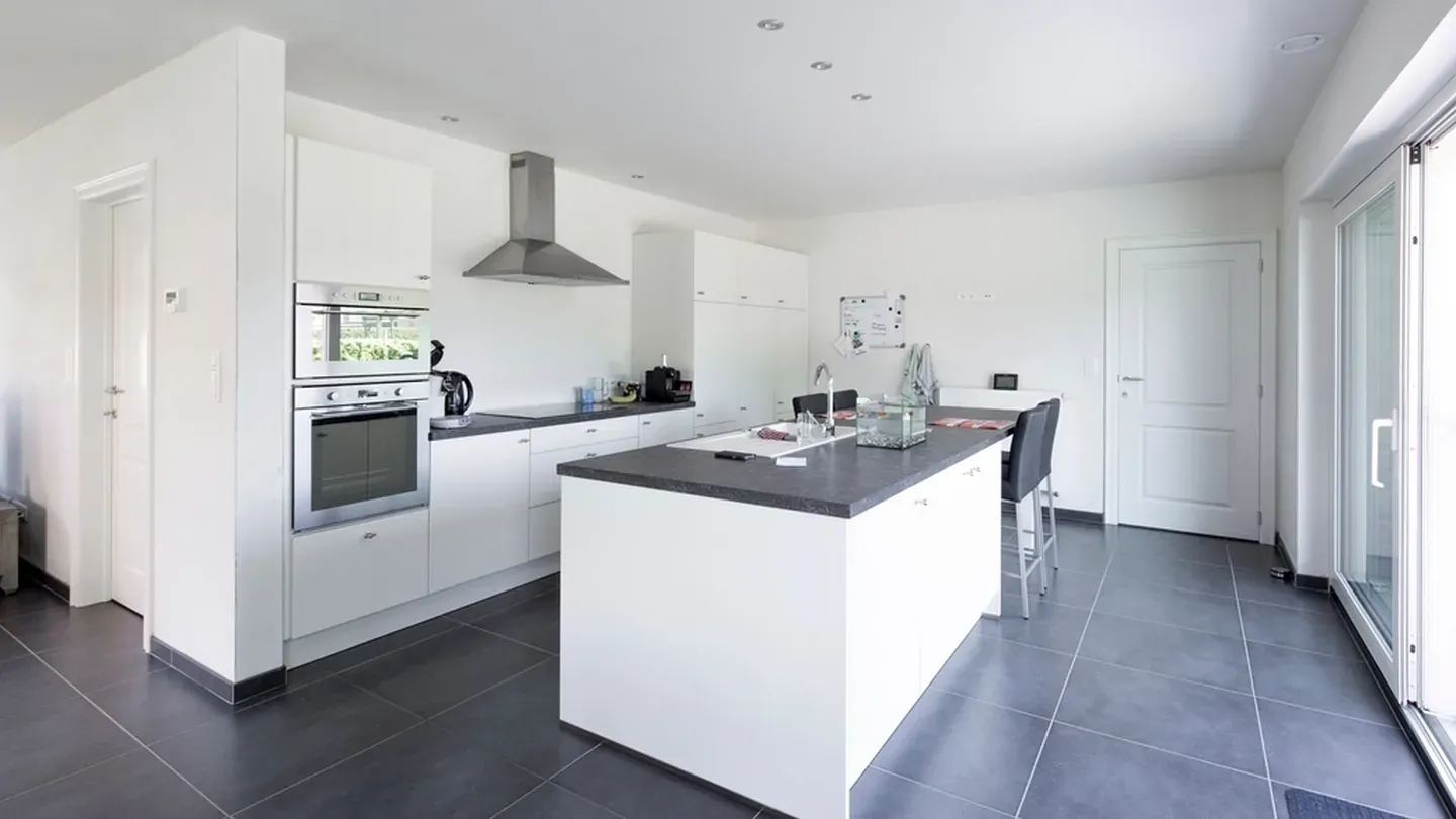Modern kitchen with a handleless white island, dark flooring and large glazed openings