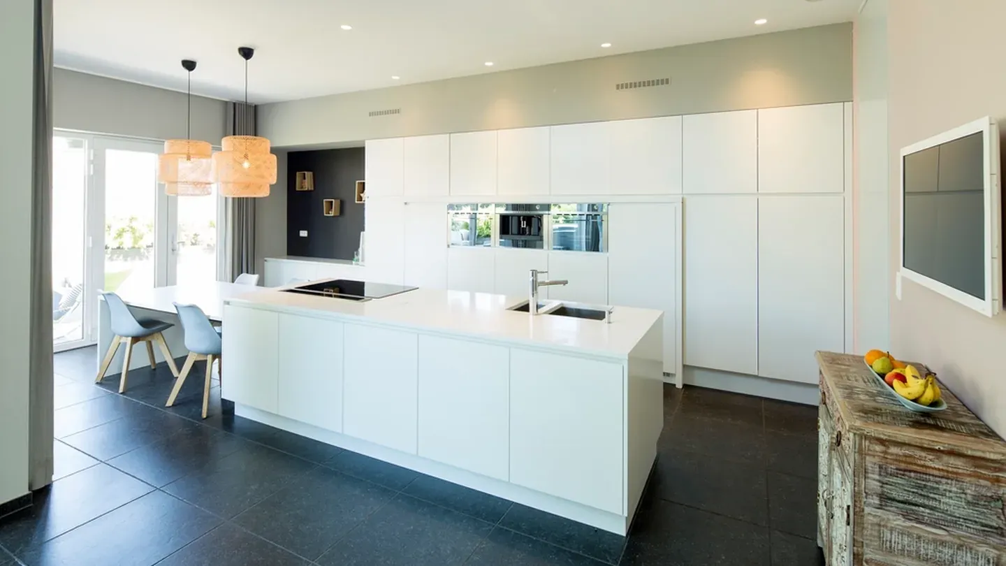 White minimalist kitchen with handleless fronts, a central island and full-height tall units